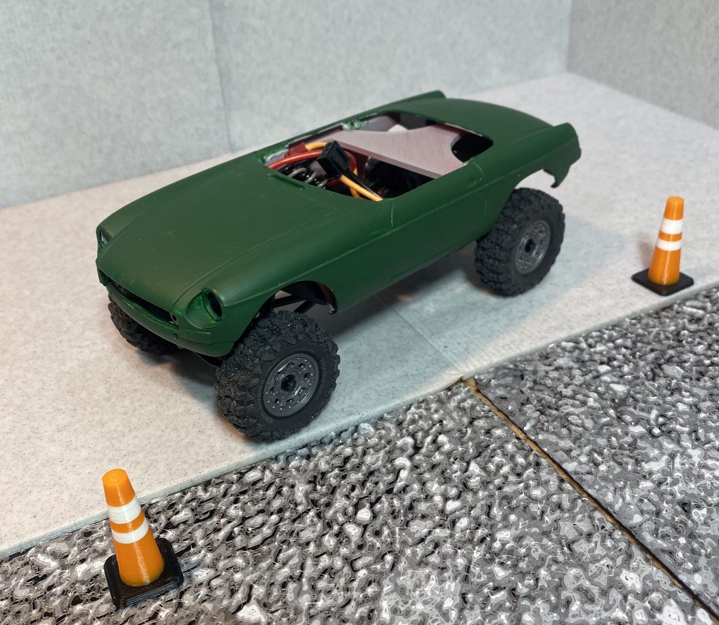 A green MGB sports car body on the crawler chassis, front three-quarter view with miniature traffic cones.