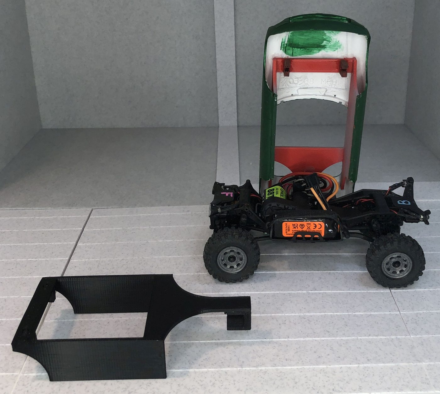 An MGB body tilted open on the bare chassis showing the shell glued inside, with a black production shell on the floor in front.