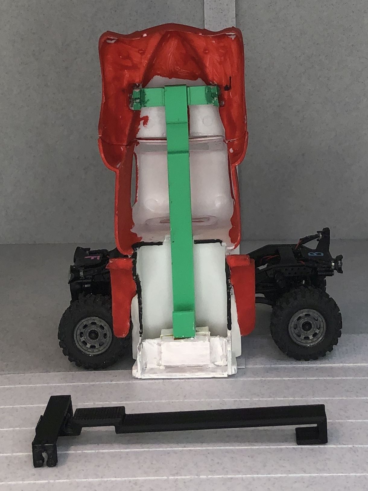 A converted body tilted up on the chassis, showing the rail, front plank and rear hook glued inside; a black production rail lies in front.